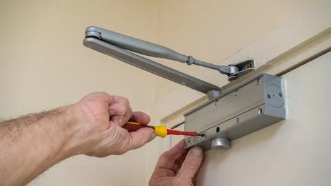 Building maintenance engineer adjusting an automatic door closer Stock Photos