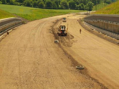 Building of new highway, scraper modify gravel surface. Man in shorts is going. Fotos de archivo