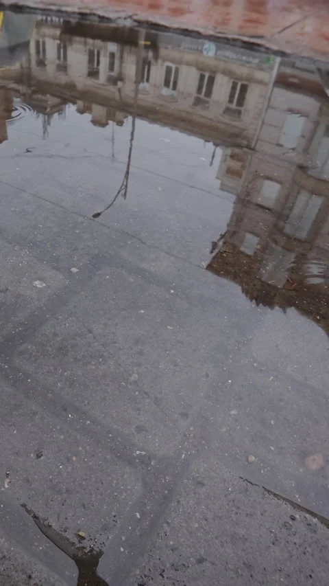 Building in old town is mirrored in puddle, drops fall onto water are blurring Stock Footage 338023755