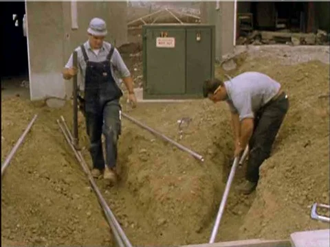 A building permit is displayed and construction workers lay pipe and hammer Vídeos de archivo 74968037