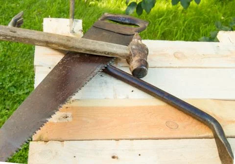 Building tools hammer, axe, hacksaw frame, lie on the light boards in the gar Stock Photos