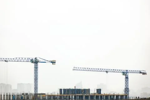 Building under construction with two tower cranes against a gray cloudy sky. Fotos de archivo