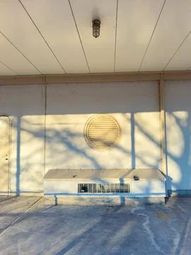 A building wall features a round vent and an air conditioning unit. Sunlight  Stock Photos
