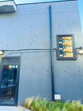 Building wall with a window and a pipe in an urban area during bright dayligh Stock Photos
