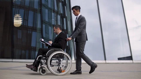 Buisness partner rolling colleague sitting on wheelchair front of modern glass Stock Footage 110201302