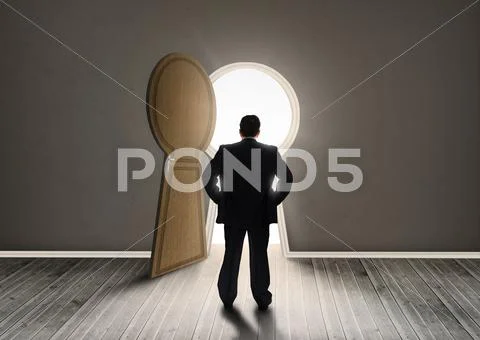 Buisnessman looking at keyhole shape door revealing light Stock Photos