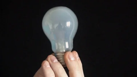 The bulb lights up in the hands of a young man,Black background Stock Footage 77109377