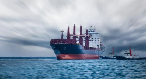 Bulk Carrier Cargo Ship Guided By Tugboat In Harbor Under Dramatic Cloudy S.. Stock Photos