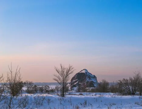 Bulk mountain and trees in a winter field under the rays of the evening sun Stock-Fotos
