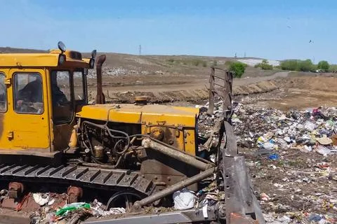 A bulldozer clears heaps of garbage in a garbage can. Work bulldozer in a l.. Stock Photos