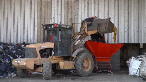 A bulldozer dumps garbage onto a conveyor belt inside a waste processing Stock Footage 210451478