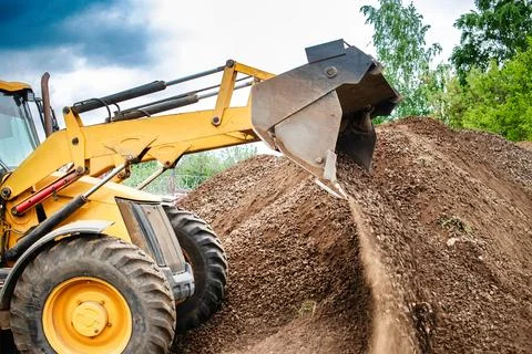 A bulldozer or a loader is actively digging dirt in a vast field, moving and Stock Photos