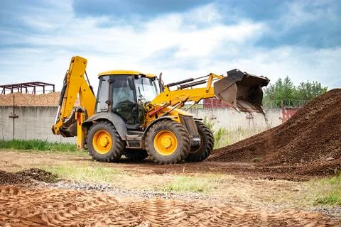 A bulldozer or a loader is actively dumping dirt into a growing pile at a con Stock Photos