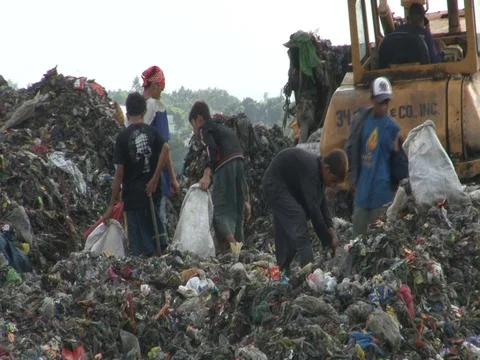 Bulldozer pushes garbage, poor people pick through it, on top of garbage dump Stock Footage 90270670