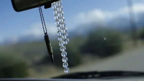Bullet casing and bracelet dangles off of a rear-view mirror in slow motion Stock Footage 92104045