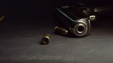 Bullets drop near handgun on table and roll away, slow motion Video stock 142852527