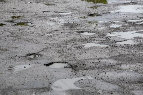 Bumpy damaged road asphalt with multiple puddles after rain at summer daytime Stock Photos