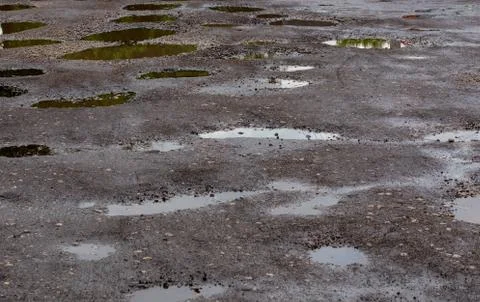 Bumpy damaged road asphalt with multiple puddles after rain at summer daytime 写真素材