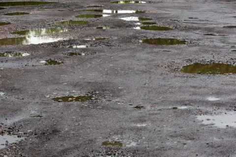 Bumpy damaged road asphalt with multiple puddles after rain at summer daytime Stock Photos