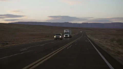 Bumpy desert road passing cars on roadtrips and a freight truck at dusk Stock Footage 244690779