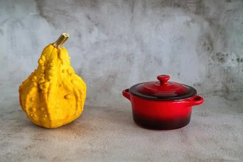 A bumpy yellow ornamental gourd stands next to a small closed red ceramic p.. Stock Photos