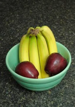 A bunch of bananas and apples inside of a fruit bowl resting on a black kitch Foto stock