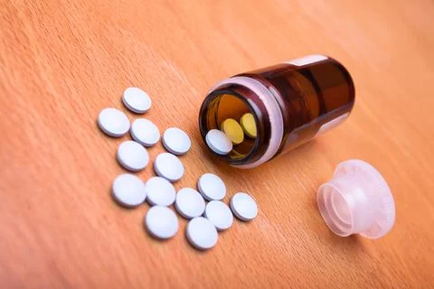 Bunch of blue pills with a bottle and a cap on an old vintage wooden table. Photos
