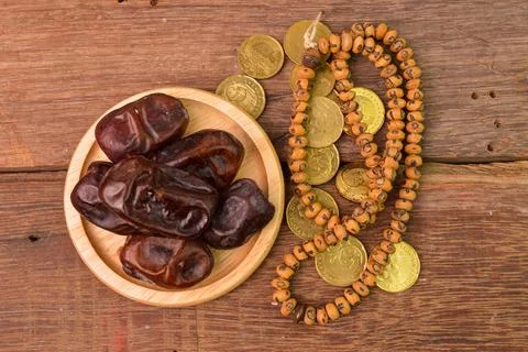 Bunch of dates, Islamic prayer beads and coins on wooden board. Ramadan karee Foto stock