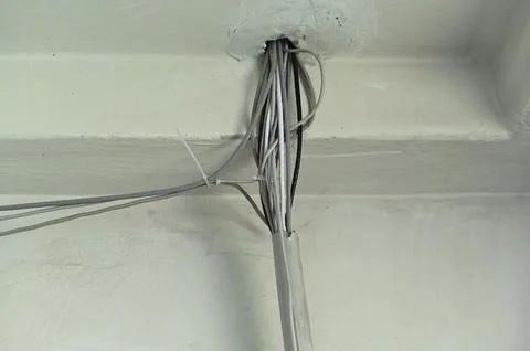 Bunch of electric cable lines hangs from hole near concrete ceiling. Stock Photos