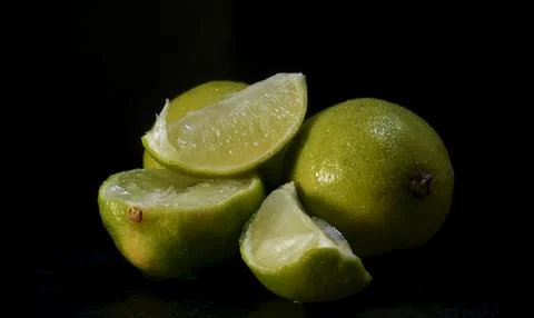 A bunch of limes on a dark background. Some limes are cut in half. Stock Photos