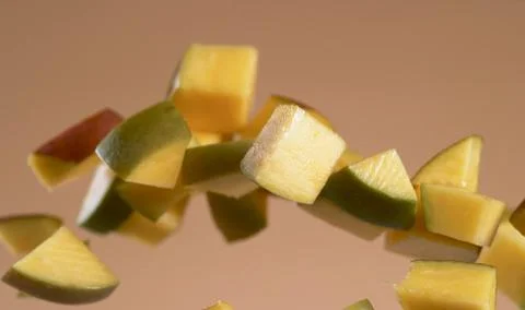 A bunch of mango cubes are suspended in mid-air against a light brown background Stock Photos