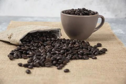 Bunch of medium roasted coffee beans out of sackcloth on marble surface Stock Photos