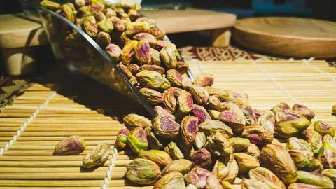 Bunch of pistachio nuts kernel scattered from a scoop on top of sushi mat w.. Foto stock