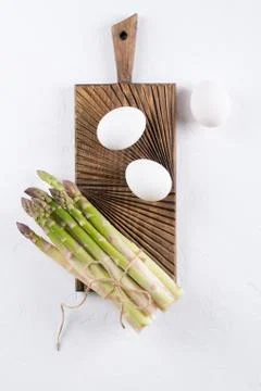 Bunch of raw fresh garden organic asparagus with eggs on wooden board. Stock Photos