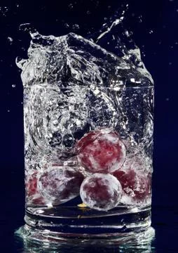 Bunch of red grapes falling down in glass with water on deep blue Foto stock