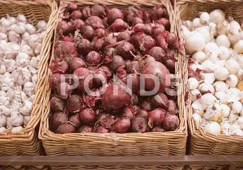 Bunch of red onion, white onion and garlic in wicker tray in supermarket Stock Photos