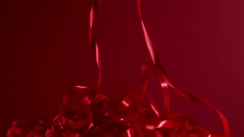A bunch of red silk shiny strips falling down on a matte red background. 4k Stock Footage 145053815
