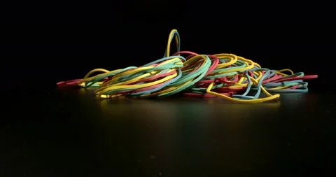 A bunch of rubber bands falling on black surface. Concept of Office Products Stock Footage 146534103