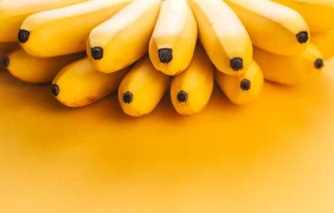 A bunch of small ripe bananas on a yellow background copy space. Stock Photos