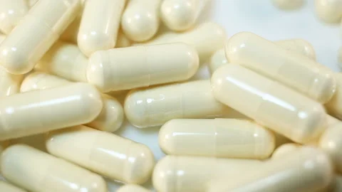 A bunch of transparent capsules with white powder inside are moved with a wooden Stock Footage 144642989