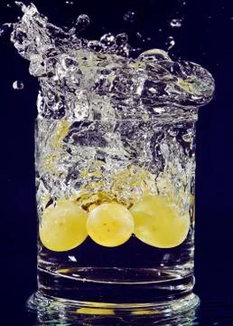 Bunch of white grapes falling down in glass with water on deep blue Foto stock