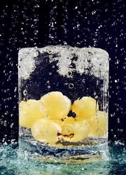 Bunch of white grapes falling down in glass with water on deep blue Stock-Fotos