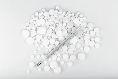 Bunch of white tablets with thermometer. Scattered pills. Stock Photos