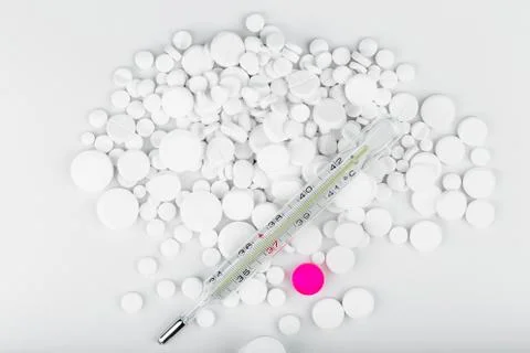 Bunch of white tablets with thermometer. Scattered pills. Stock Photos