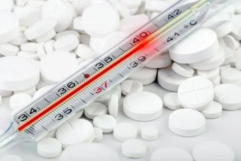 Bunch of white tablets with thermometer. Scattered pills. Stock Photos