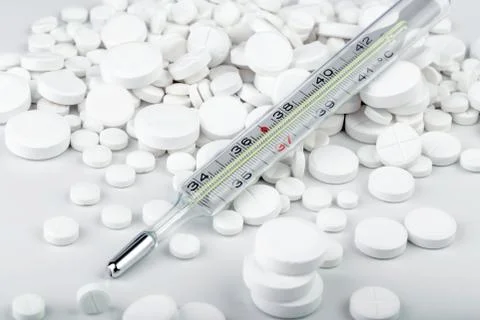Bunch of white tablets with thermometer. Scattered pills. Stock Photos