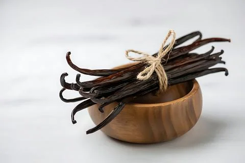 A bundle of aromatic vanilla beans in a wooden bowl on a white wood table. .. Stock Photos