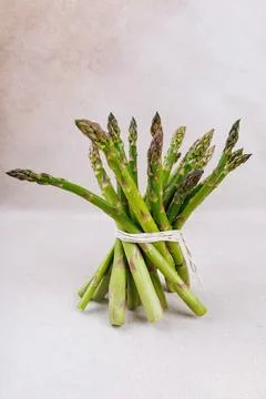Bundle of asparagus tied with string, placed vertically on textured surface Stock Photos