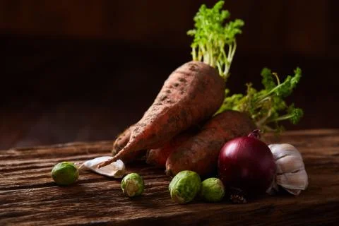 Bundle of carrots with soil over rustic wooden background, side view, close-up Stock Photos