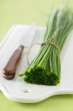 A bundle of chives and a knife on a chopping board Stock Photos